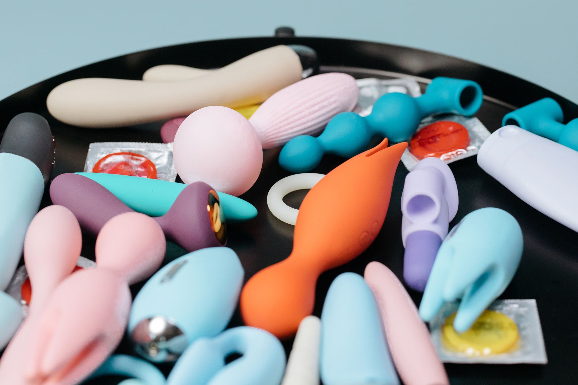 Due mani che tengono vibratori silicone rosa e blu su sfondo pastello