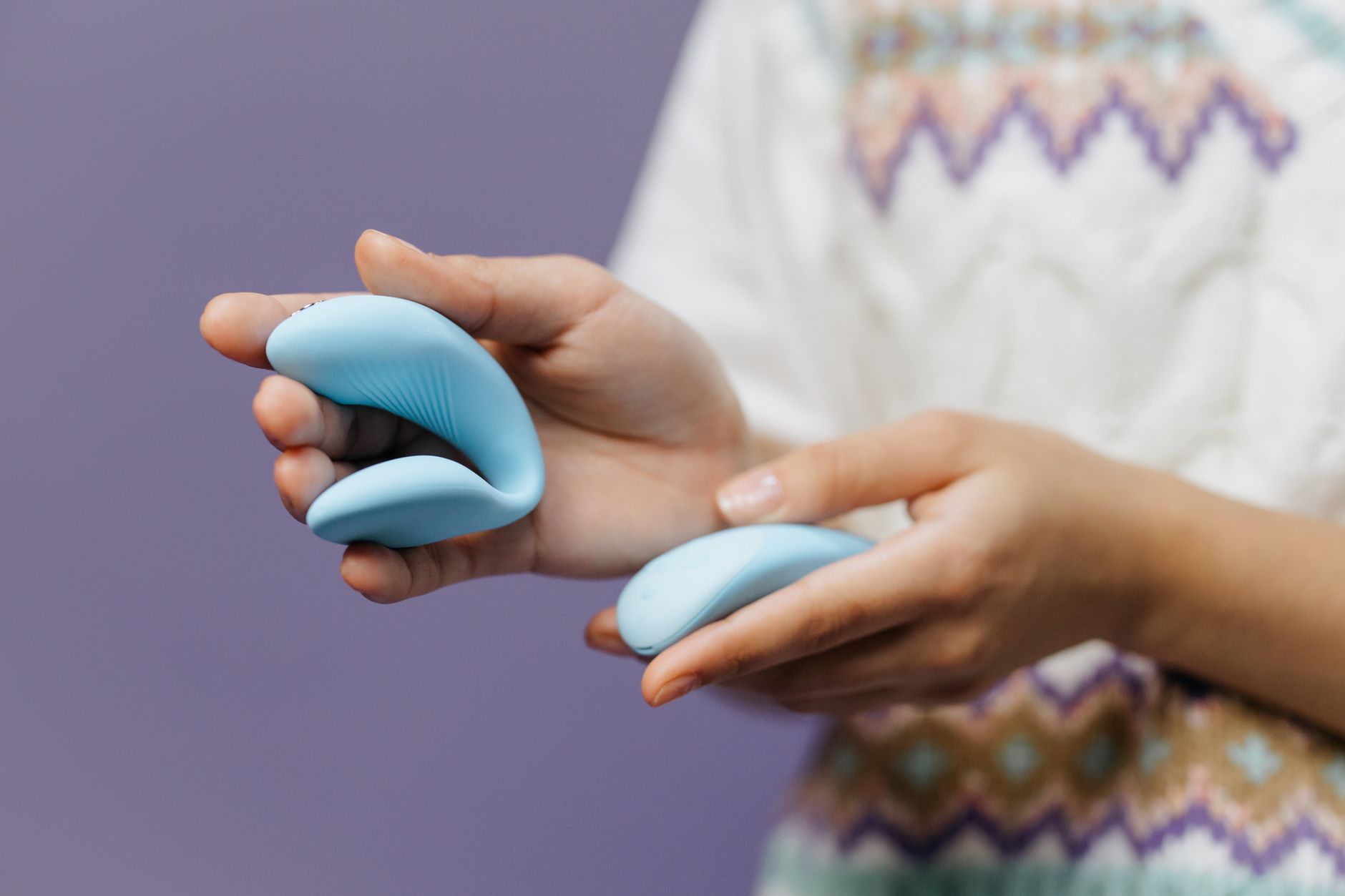 Mani che tengono un vibratore blu elegante su uno sfondo viola.