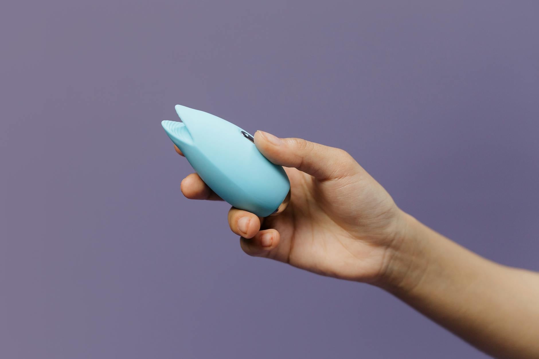 Un vibratore in silicone blu tenuto in mano contro uno sfondo viola, che promuove l'amore per se stessi e la sessualità
