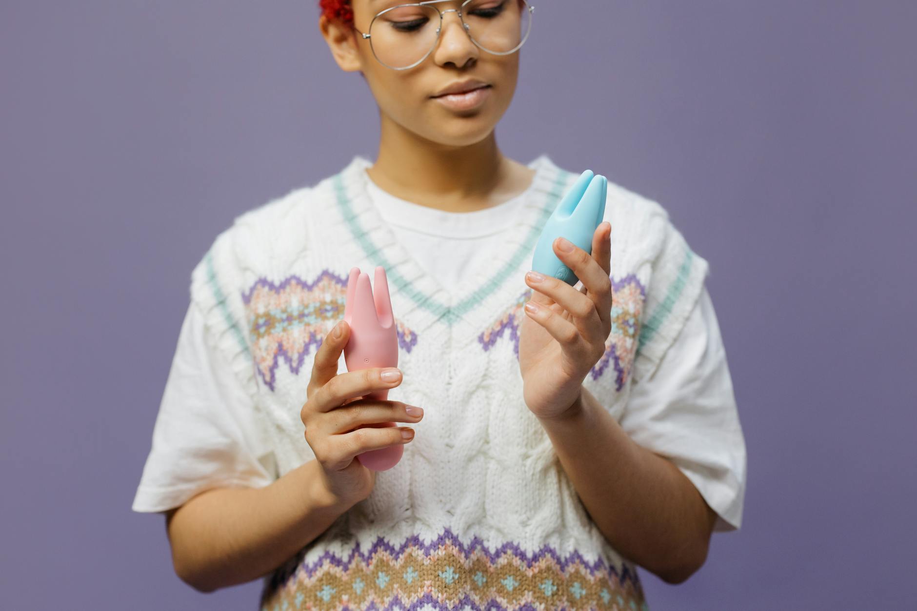 Donna con occhiali che tiene in mano vibratori in silicone colorati in atteggiamento contemplativo.