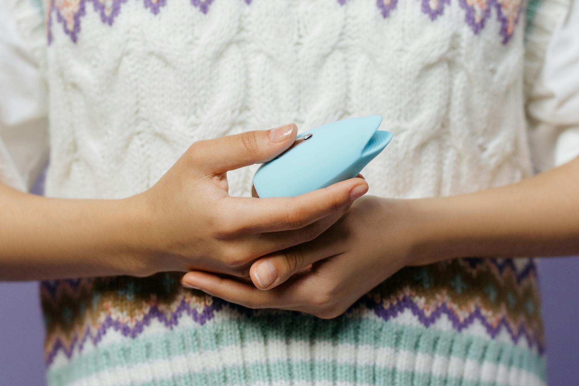 Primo piano delle mani che tengono un vibratore blu contro una maglia in lana.