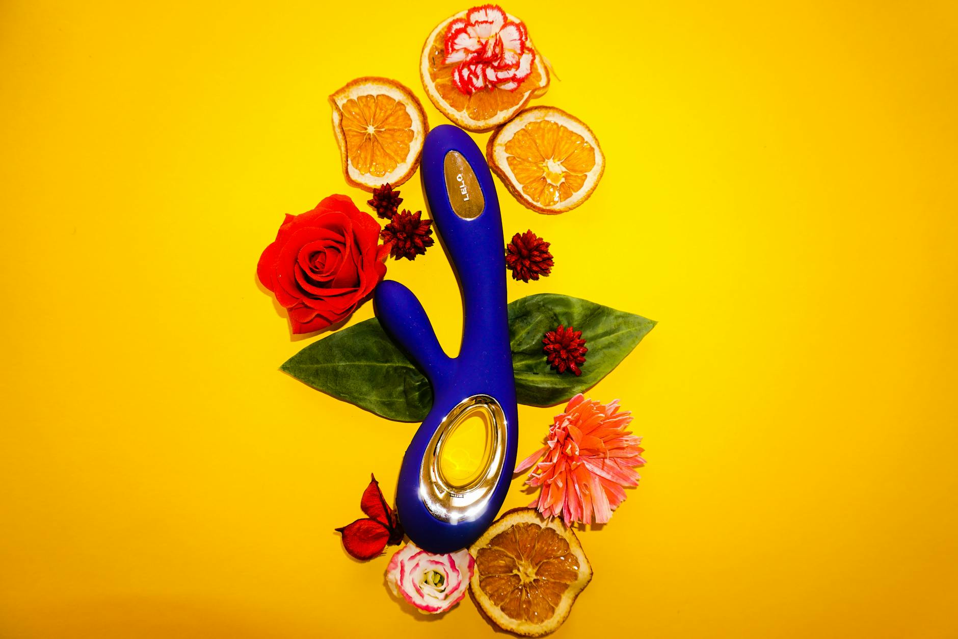 Vibratore blu del limone circondato da fiori e fette d'arancia su sfondo giallo