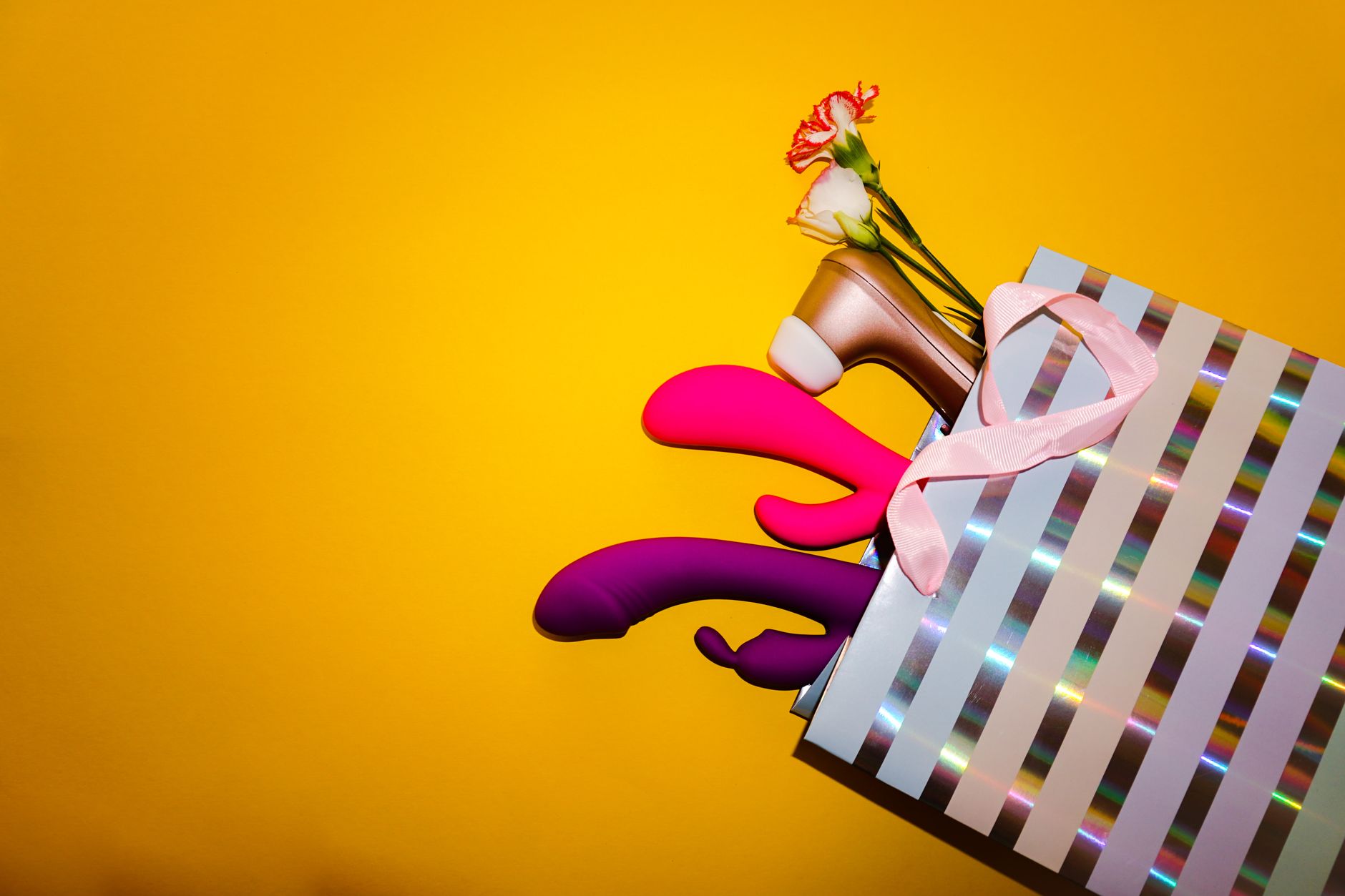 Vibratori colorati al limone con fiori in una borsa regalo olografica su sfondo giallo brillante