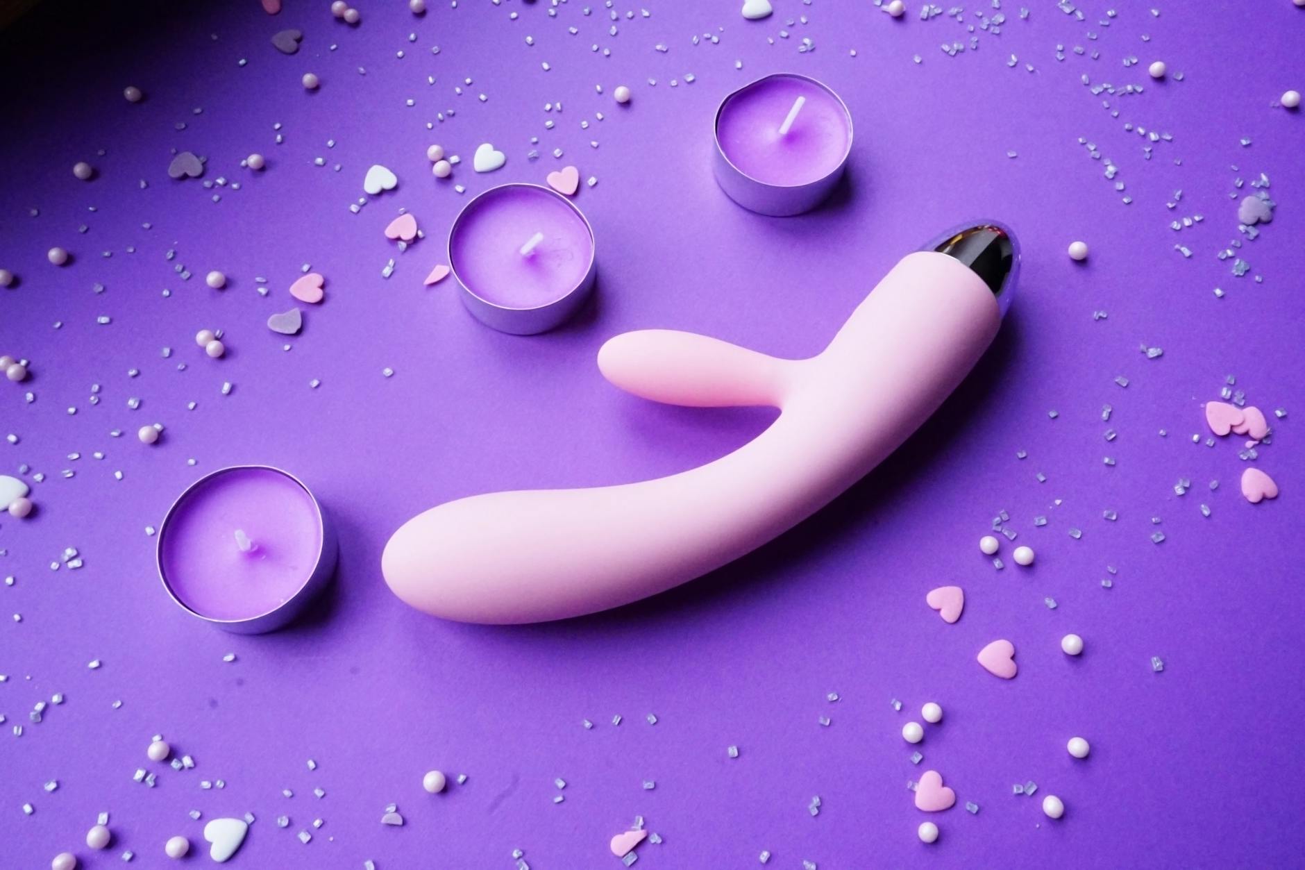 Vibratore rosa su sfondo viola con coriandoli a cuore e candele per un'atmosfera romantica